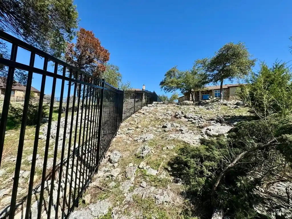 Black iron fence along a rocky hill, separating two Austin back yards.