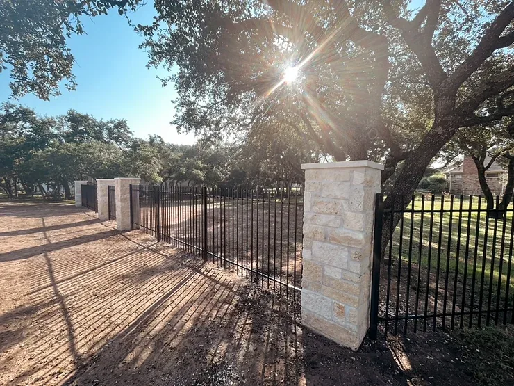 Black iron fence with stone pillars surrounding an Austin, Texas home.