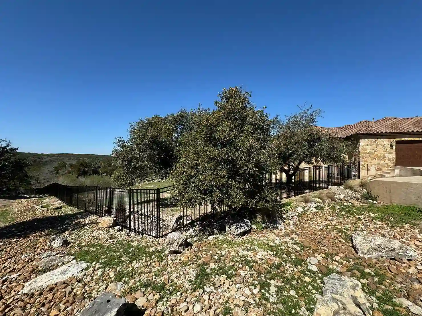 Custom black iron fence enclosing a back yard on a rocky hill.