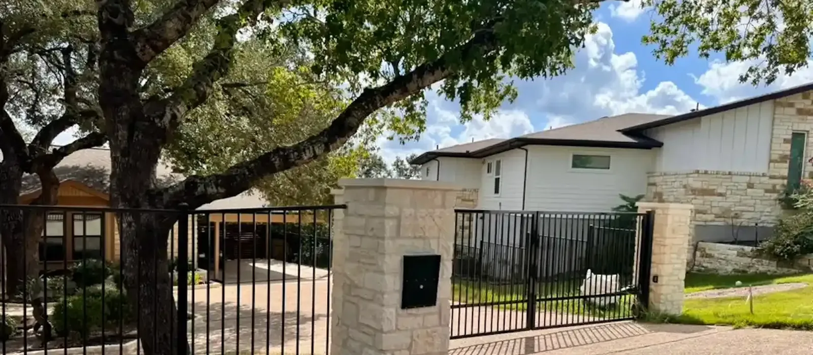 Black iron fence and driveway gate between limestone columns with a stone mailbox column under a mature live oak, built by Sagamore Fence & Deck