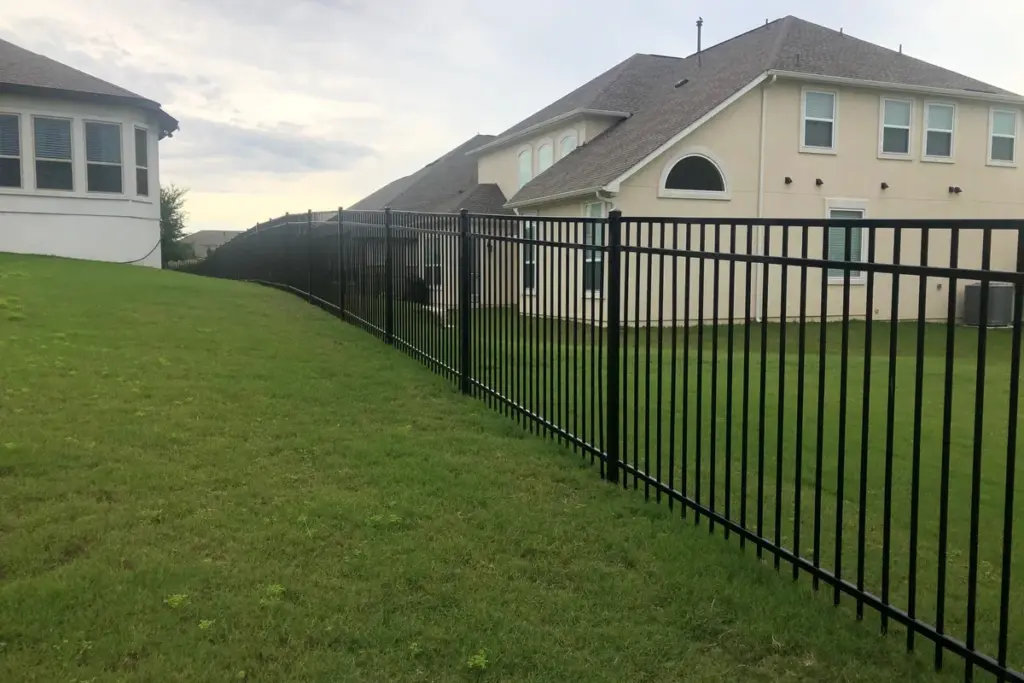 Black ornamental iron fence along a sloped lawn beside a two-story home