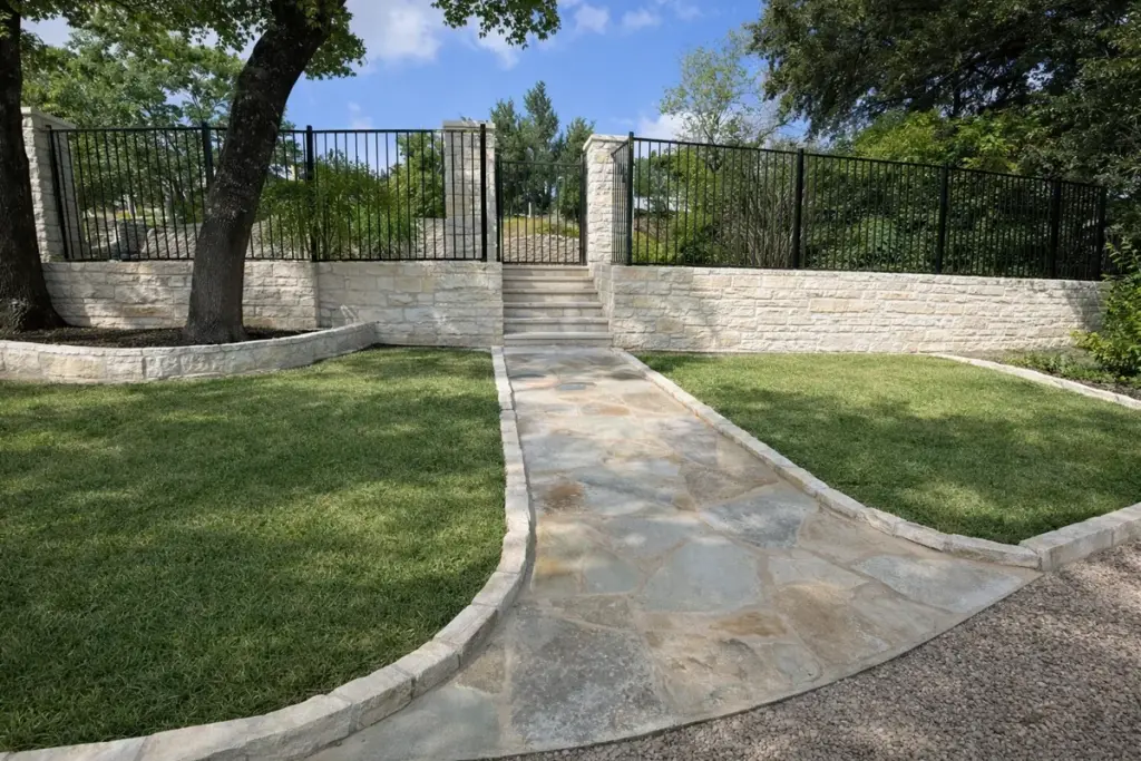 Black iron fence panels on a white limestone wall with stone columns at the top of a flagstone front walkway