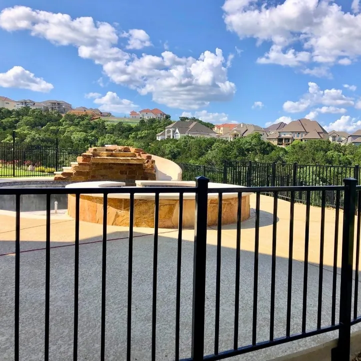 Black flat-top iron pool fence around a pool deck with homes on the hill behind it