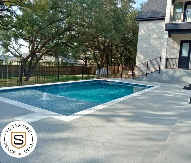Black iron pool fence and stair railing around a concrete pool deck