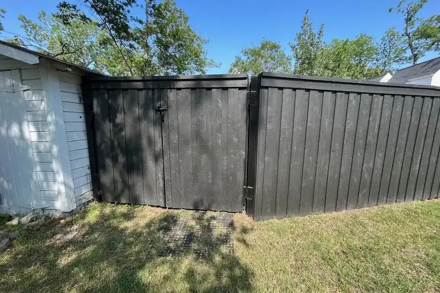 Black-stained wood privacy fence with a matching walk gate beside a white home