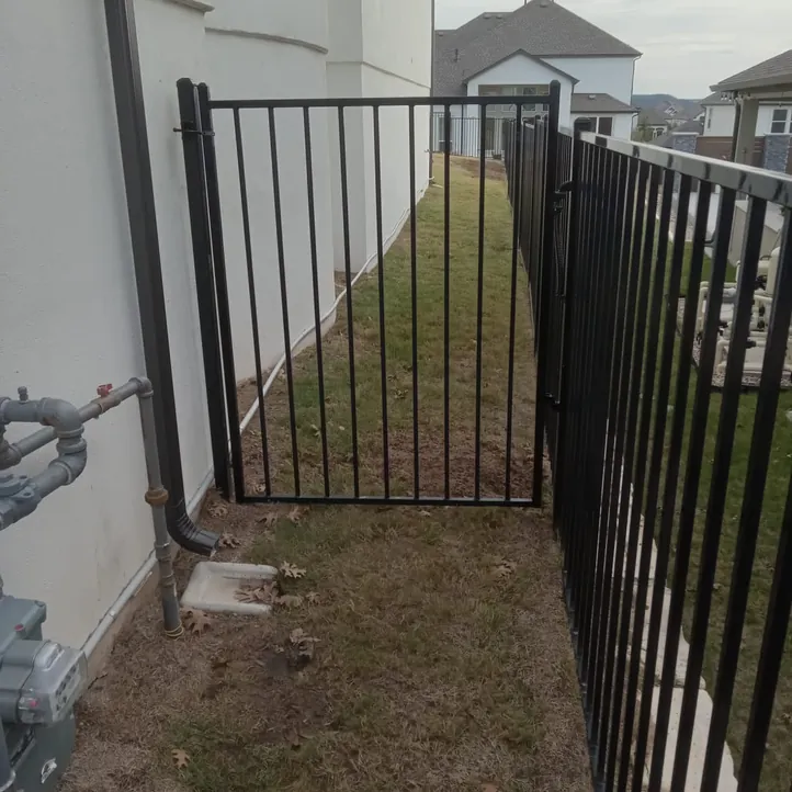 Black flat-top iron fence panels and a matching walk gate along a narrow side yard