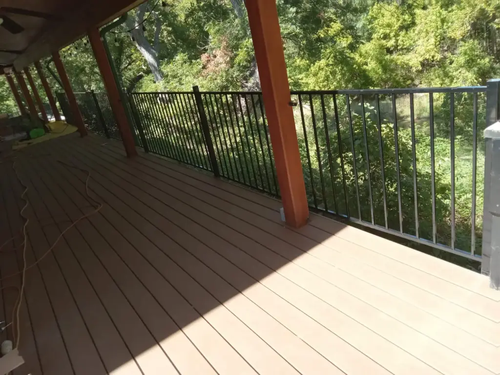 Covered deck with tan decking, cedar posts and black metal railing overlooking trees, by Sagamore Fence & Deck for Cedar Park, TX homes