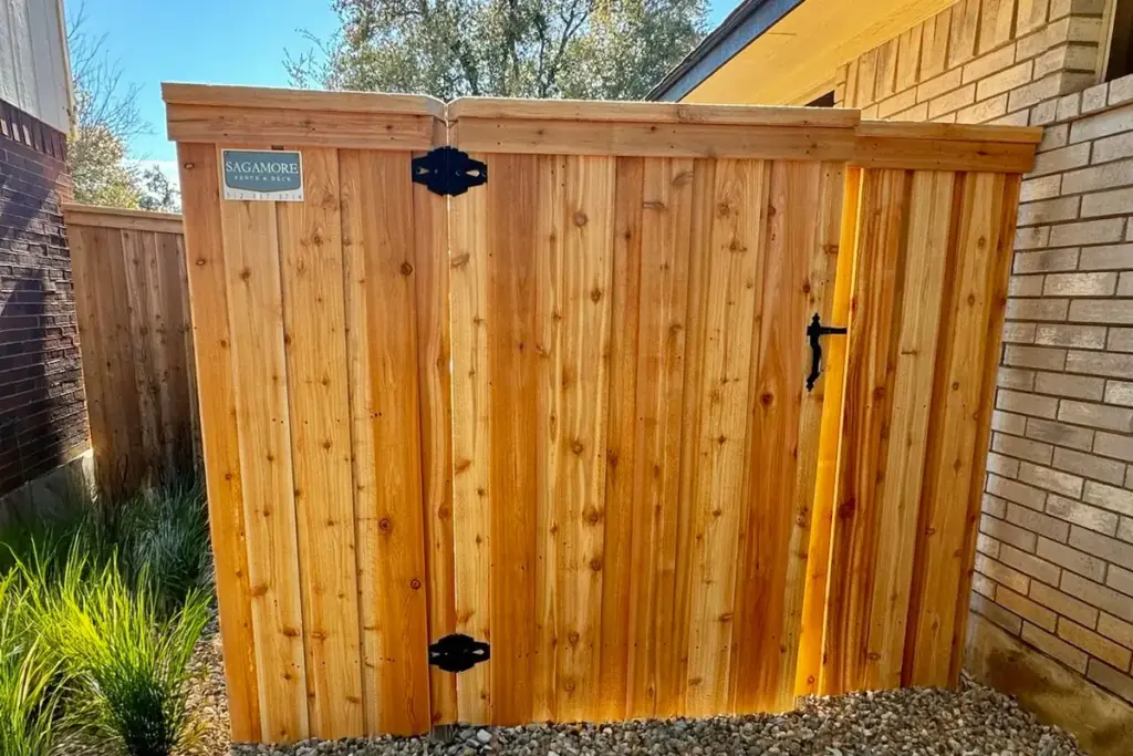 Cedar walk gate with black hardware beside a brick home and gravel path