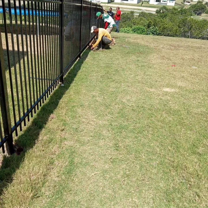 Sagamore Fence & Deck crew installing a black three-rail iron fence along a sloped lawn