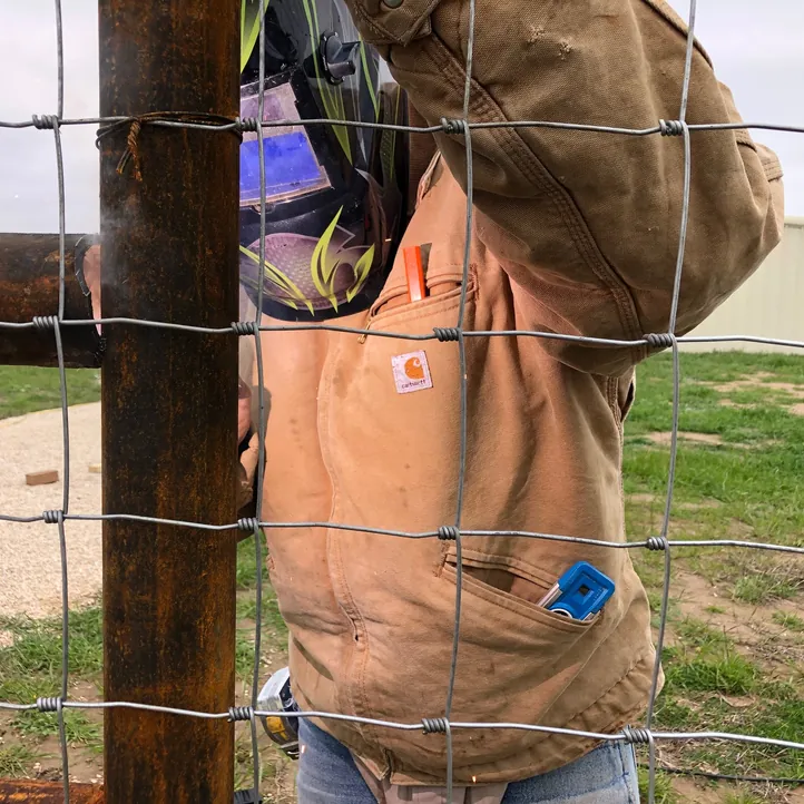 Sagamore Fence & Deck crew member welding a steel pipe fence post with woven wire attached