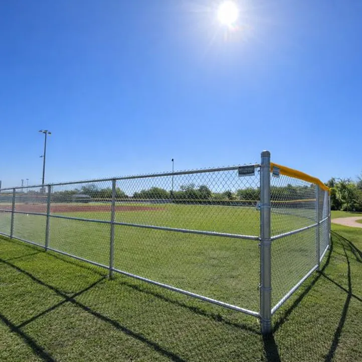 Galvanized chain link fence with a yellow top cap around a grass ball field