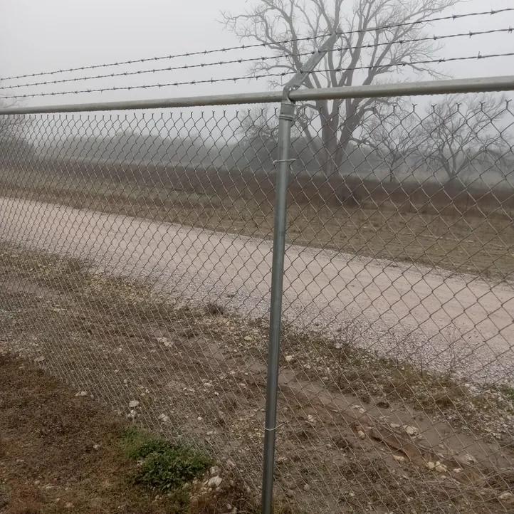 Galvanized chain link security fence topped with barbed wire along an open field