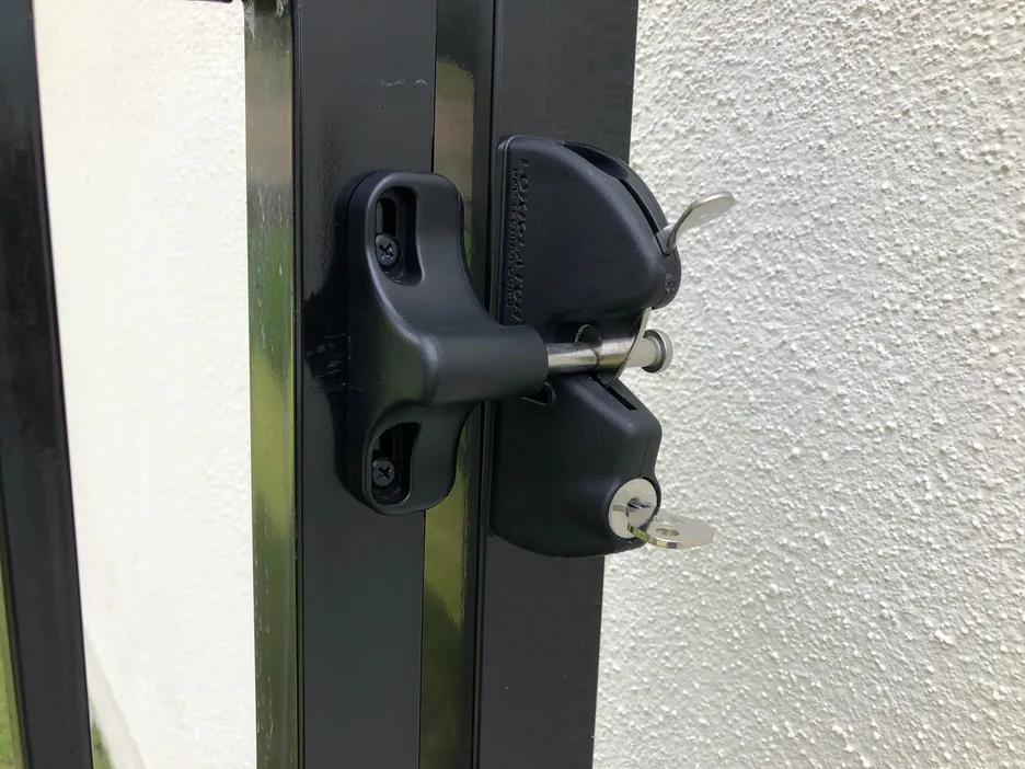 Close-up of a keyed, self-latching gate latch on a black metal gate