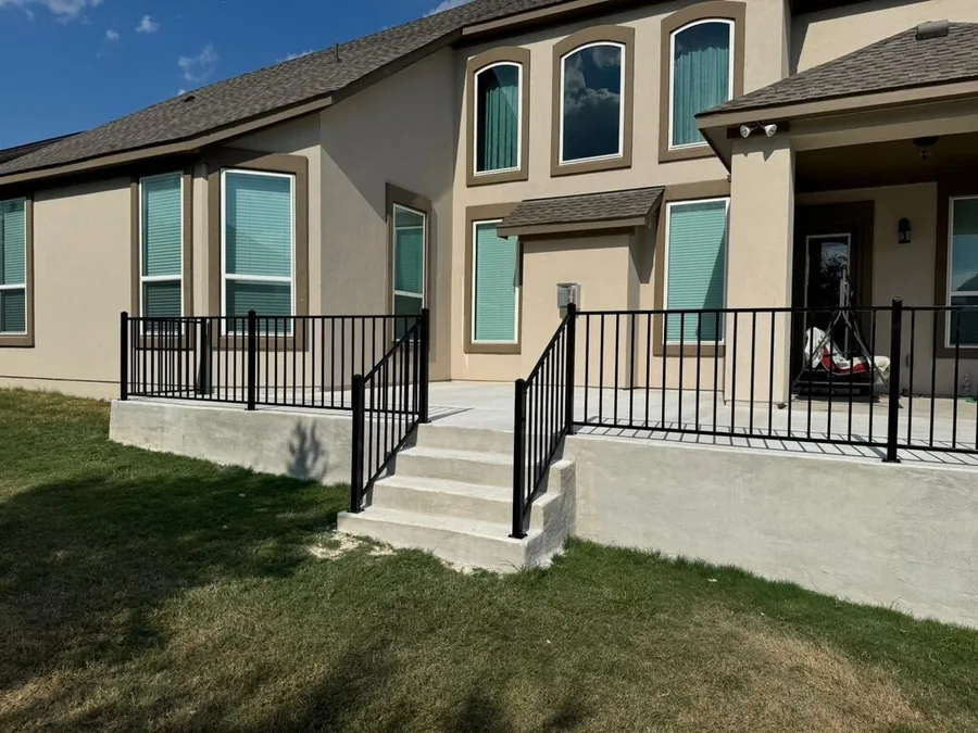 Black ornamental iron fence along a raised concrete patio with steps, built by Sagamore Fence & Deck for Lago Vista, TX homes