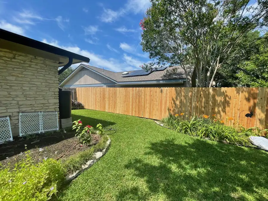 Wood privacy fence around a green backyard with flower beds, by Sagamore Fence & Deck for Liberty Hill, TX homeowners