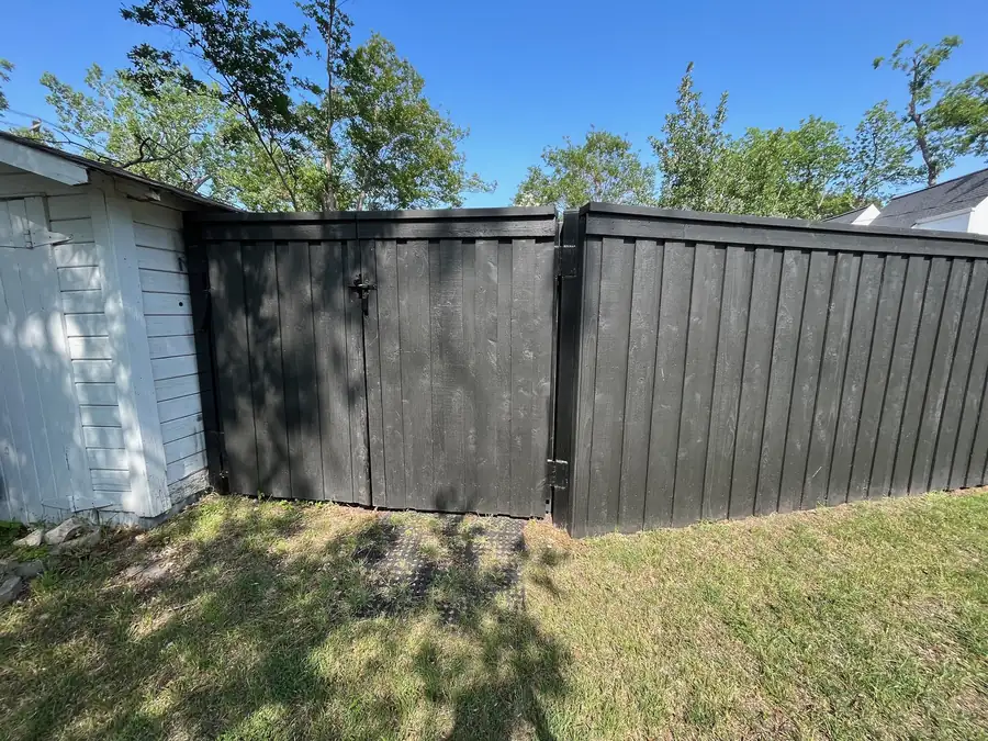 Black-stained wood privacy fence with a matching walk gate beside a white shed, by Sagamore Fence & Deck for Manor, TX homes