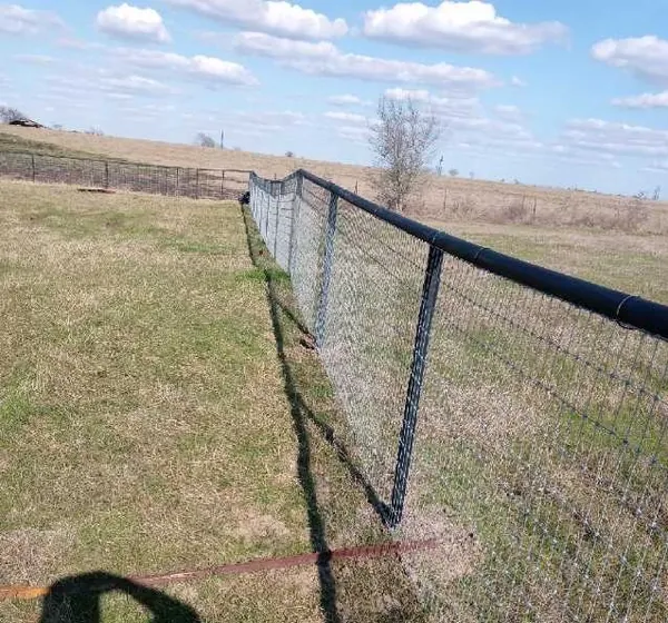 Pipe-rail fence with wire mesh along an open pasture
