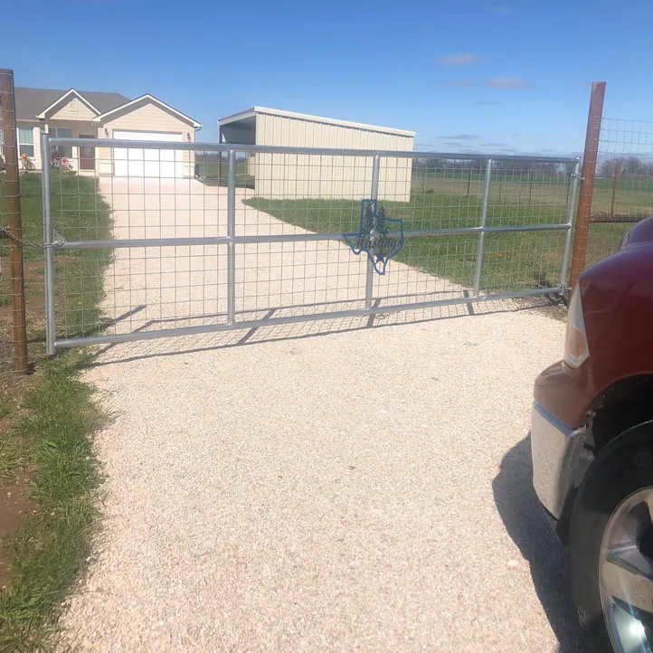 Pipe-frame double ranch gate with wire panels across a gravel driveway
