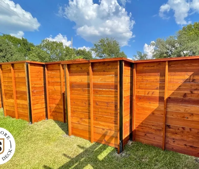 Stained horizontal wood fence with black posts wrapping a backyard