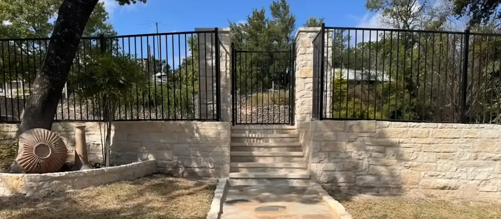 Black iron fence and walk gate on a limestone retaining wall with stone steps and a flagstone path, built by Sagamore Fence & Deck